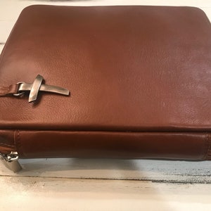 May include: A brown leather Bible cover with a silver cross accent and a zipper closure.