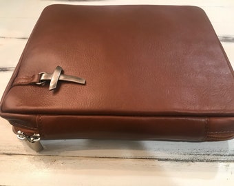 May include: A brown leather Bible cover with a silver cross accent and a zip closure.