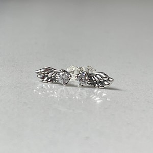 Könnte beinhalten: Ein Paar silberne Ohrringe mit Flügeldesign und einem klaren Kristall in der Mitte jedes Flügels.