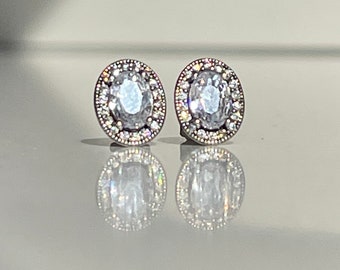 May include: A pair of silver oval-shaped earrings with a clear crystal center surrounded by smaller crystals.