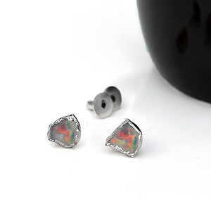 K&ouml;nnte beinhalten: Ein Paar Ohrstecker mit unregelm&auml;&szlig;igen, roh geschliffenen Opalen, die lebhafte rote, orangefarbene und gr&uuml;ne Farbspiele zeigen. Jeder Opal ist in eine texturierte, silberfarbene Metallfassung eingefasst, mit passenden Metallverschl&uuml;ssen daneben.