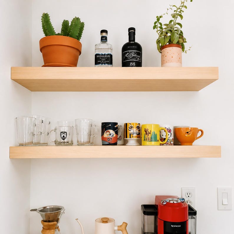 Pode incluir: Duas prateleiras flutuantes de madeira clara montadas numa parede branca. A prateleira superior cont&eacute;m um cato verde num vaso de terracota, uma garrafa de tequila Lunazul, uma garrafa preta e uma planta num vaso salpicado. A prateleira inferior exibe v&aacute;rios copos de vidro.