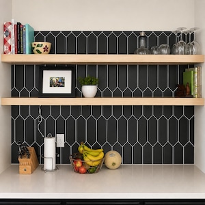 Pode incluir: Duas prateleiras flutuantes de madeira clara montadas contra um revestimento de azulejos pretos em formato de estaca. As prateleiras cont&ecirc;m livros, uma tigela floral, copos, uma foto emoldurada, uma pequena planta e um bloco de madeira para facas.