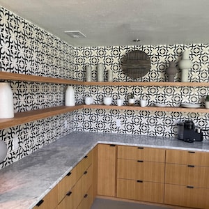 Pode incluir: Uma cozinha com arm&aacute;rios de madeira clara com ferragens pretas, bancada de m&aacute;rmore cinza e prateleiras de madeira abertas. As paredes s&atilde;o revestidas com azulejos quadrados com padr&otilde;es em preto e branco. V&aacute;rios vasos e canecas est&atilde;o expostos.