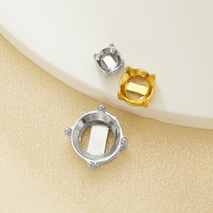 May include: Three metal jewelry settings in silver and gold tones. The settings are round with prongs and a flat base. One setting is silver, another is gold, and a smaller silver setting is also present.