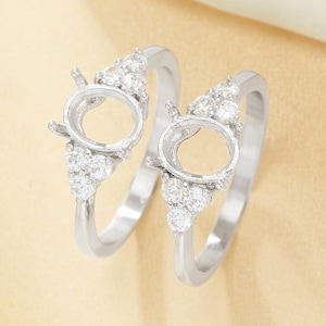 May include: Two silver rings with oval settings and small, clear accent stones. The rings have a delicate design, with a cluster of stones on each side of the oval setting. The rings are displayed on a light-colored surface.