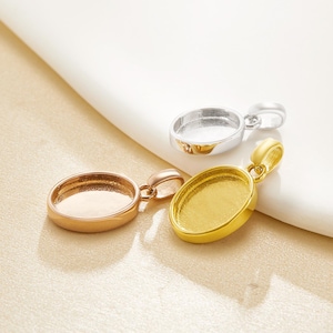 Puede incluir: Tres bandejas de colgantes ovalados en oro, oro rosa y plata. Cada colgante tiene un lazo para una cadena y un área empotrada para sostener una piedra u otro adorno. Los colgantes se exhiben sobre una superficie blanca y beige.