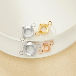 May include: Four metal jewelry clasps in silver, gold, and rose gold tones are arranged on a white surface. Each clasp has a circular design with small loops for attaching jewelry components. The clasps are likely used for necklaces or bracelets.