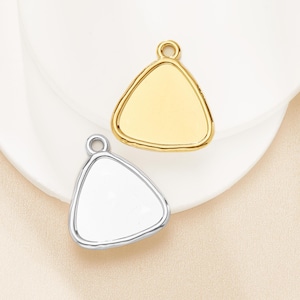 May include: Two triangular pendants, one gold-toned and one silver-toned, each with a rounded edge and a small loop at the top. The pendants are displayed on a white surface.