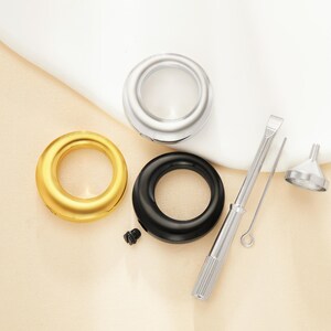 Puede incluir: Un surtido de componentes metálicos, que incluyen un anillo plateado, un anillo dorado y un anillo negro. También se incluyen un pequeño embudo plateado, un destornillador y una pequeña varilla metálica. Los artículos están dispuestos sobre una superficie beige claro.