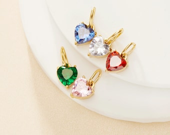 May include: Five gold heart-shaped charms with different colored gemstones. The charms feature a blue, white, red, green, and pink gemstone.