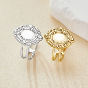 May include: Two adjustable rings with a round, ornate design. The ring on the left is silver, and the ring on the right is gold.