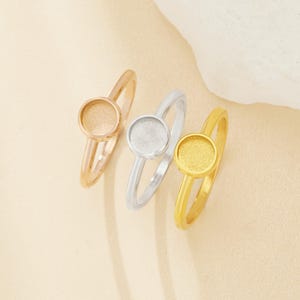 May include: Three rings with round, textured metal settings. The rings are gold, silver, and rose gold.