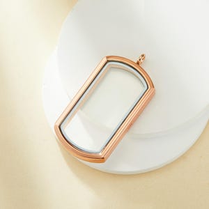 May include: A rose gold locket pendant with a clear glass insert. The locket is shaped like a rectangle with rounded corners.
