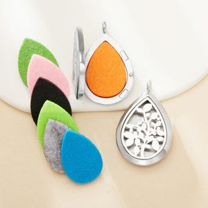 May include: Silver teardrop-shaped essential oil diffuser pendants with colorful felt pads. One pendant has an orange pad, another has a floral design. The felt pads are green, pink, black, light green, gray, and blue.