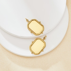 Peut inclure: Deux breloques pendantes en métal doré de forme rectangulaire avec une bordure perlée. Les breloques ont une surface vierge pour la personnalisation.