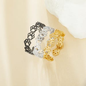 Op de afbeelding: Drie verstelbare ringen met een pootprint ontwerp. De ringen zijn goud, zilver en zwart.