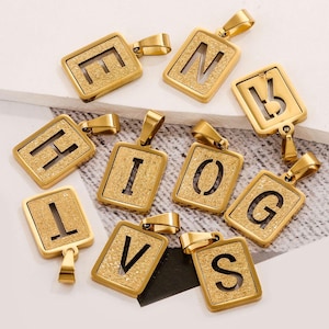 May include: Ten gold-colored metal pendants with different letters of the alphabet. Each pendant is a square with a cutout letter and a textured surface.