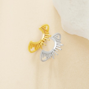 May include: Two gold and silver ear cuffs with a sunburst design. The cuffs are open and have a delicate, intricate design.