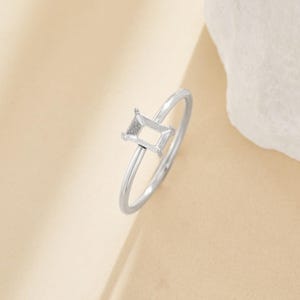 May include: A silver ring with an empty rectangular setting for a gemstone.