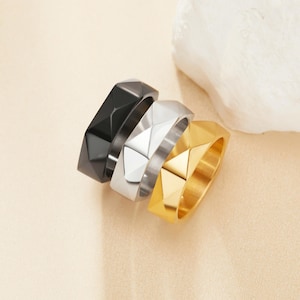 May include: Three geometric rings in black, silver, and gold. The rings are stacked on top of each other.
