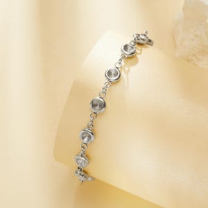 Op de afbeelding: Een zilveren armband met een reeks cirkelvormige, bezel-set elementen. De armband heeft een delicaat kettingontwerp en een veilige sluiting. De cirkelvormige elementen hebben een reflecterende, gepolijste afwerking, waardoor een subtiele glans ontstaat.
