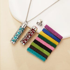 May include: A silver essential oil diffuser necklace with two cylindrical pendants, one teal and one red, both with heart-shaped cutouts. Includes a set of colorful felt pads for scent diffusion.
