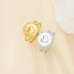 May include: Two gold and silver rings with a heart design. The rings are stacked on top of each other.