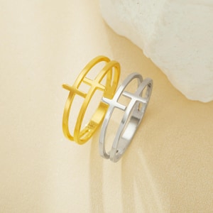 Puede incluir: Dos anillos con un diseño de cruz. Un anillo es de oro y el otro es de plata.