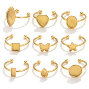 Peut inclure: Ensemble de dix bagues réglables dorées avec des formes de sertis vides différentes. Les sertis sont ovales, en forme de cœur, circulaires, carrés, en forme de papillon, en forme d'étoile, rectangulaires, en forme de goutte et deux cercles.