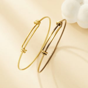 May include: Two gold-toned adjustable bangle bracelets. The bracelets are made of thin metal and have a simple, minimalist design.