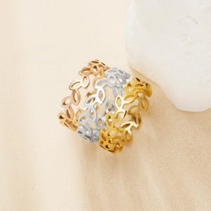 May include: Three leaf-patterned rings in gold, silver, and rose gold. The rings are made of metal and have an openwork design. The rings are stacked together, showcasing the different colors and styles. The rings are on a neutral background.
