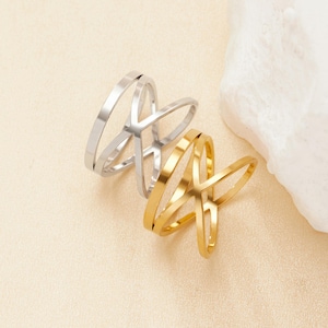 Puede incluir: Dos anillos, uno plateado y otro dorado, con un diseño geométrico abierto. Los anillos están apilados uno encima del otro.