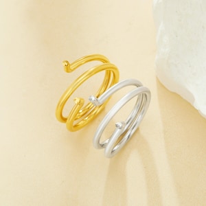 Könnte beinhalten: Zwei Spiralringe, einer in Gold und einer in Silber, liegen übereinander. Die Ringe sind schlicht und elegant.
