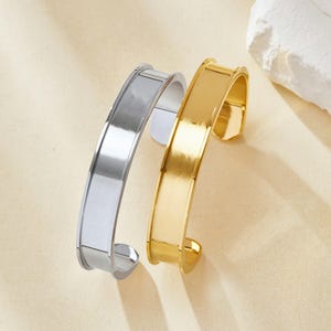 Può includere: Due braccialetti semplici, uno in argento e uno in oro, con una finitura liscia e lucida. I braccialetti sono aperti alle estremità e hanno una forma leggermente curva.