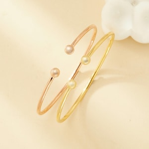 May include: Two gold bangles with pearl accents. One bangle is rose gold and the other is yellow gold.