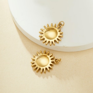 Può includere: Due ciondoli a forma di sole dorati con una superficie testurizzata. I ciondoli sono su uno sfondo bianco.