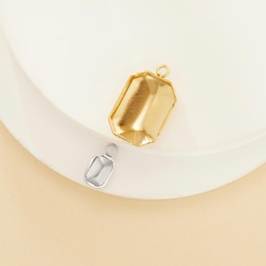 Puede incluir: Dos bandejas de colgante de metal dorado con forma rectangular y borde biselado. Las bandejas están diseñadas para contener un cabujón de fondo plano u otro adorno.