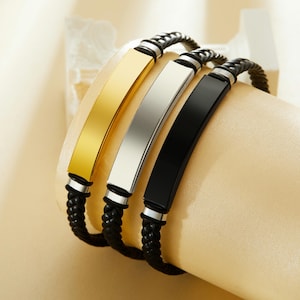 Könnte beinhalten: Drei geflochtene Lederarmbänder mit Metallplatten. Die Platten sind golden, silber und schwarz.