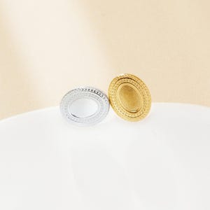 May include: Two oval-shaped metal earrings with a decorative border. One earring is silver and the other is gold.