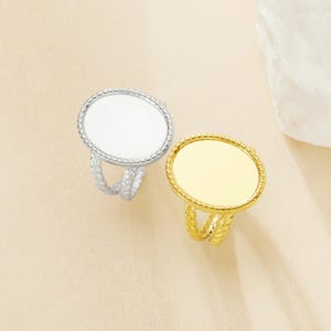 Puede incluir: Dos anillos ajustables con placas redondas de metal en blanco. El anillo de la izquierda es plateado y el anillo de la derecha es dorado.