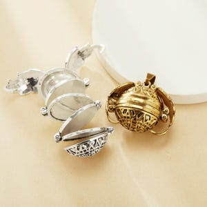 Può includere: Due ciondoli a medaglione in argento e oro. Il medaglione d'argento è aperto e ha quattro strati. Il medaglione d'oro è chiuso e ha un design dettagliato.