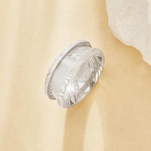 May include: A silver ring with a textured, grooved design. The ring is made of metal and has a polished finish.
