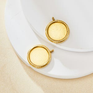 Op de afbeelding: Twee rond gouden hanger-schalen met een getextureerde rand. De schalen zijn leeg en klaar voor hars of andere versieringen.