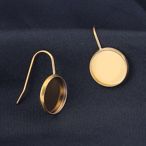 Puede incluir: Un par de bases de pendientes de color dorado con biseles redondos abiertos. Los ganchos de los pendientes son simples y los biseles están listos para ser rellenados con resina u otros materiales.