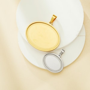 Puede incluir: Dos colgantes ovalados de metal, uno dorado y otro plateado, con una superficie lisa y un bucle en la parte superior para sujetar una cadena.