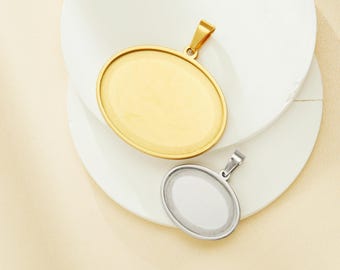 May include: Two oval-shaped metal pendant blanks, one gold and one silver, with a smooth surface and a loop at the top for attaching a chain.