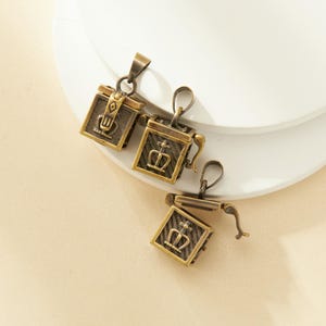 May include: Three antique gold-toned metal pendants shaped like small boxes with hinged lids. Each box has a crown and cross design.