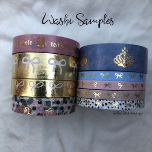 May include: A collection of washi tape samples featuring gold foil, floral, and crown designs. The tape is arranged in two stacks, with the text "Golden State Boutique" visible on the bottom of the right stack.