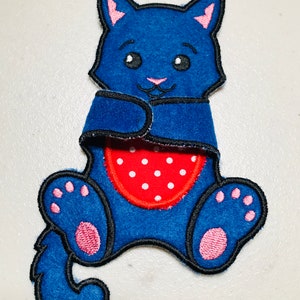 Op de afbeelding: Blauwe vilt kattenapplicatie met roze oren en poten. De kat houdt een rood vilt hart vast met witte stippen.